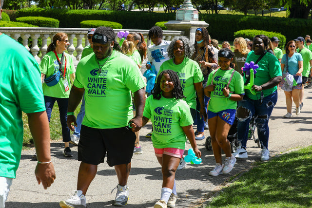 A crowd walks together around Wade Lagoon, many people are wearing matching bright green White Cane Walk shirts. 